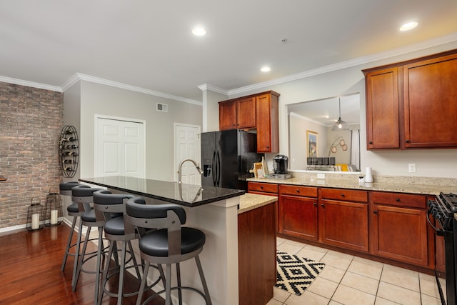 kitchen featuring stone counters, light hardwood / wood-style flooring, a kitchen bar, black appliances, and ornamental molding