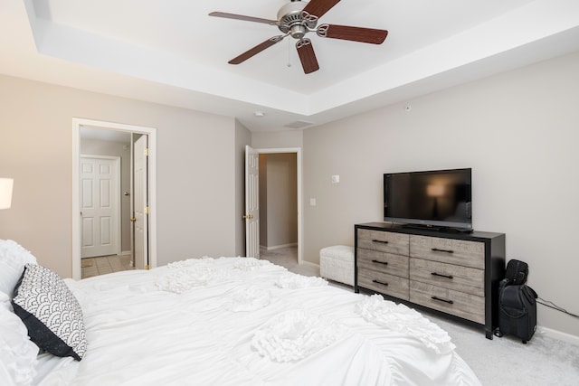 bedroom featuring ceiling fan, light colored carpet, and a tray ceiling