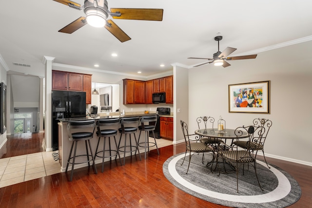 kitchen with a breakfast bar area, crown molding, dark wood-type flooring, and black appliances