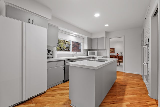 kitchen with gray cabinetry, sink, light hardwood / wood-style flooring, white appliances, and a kitchen island