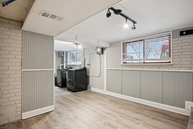 basement featuring rail lighting, washing machine and dryer, brick wall, wood walls, and light wood-type flooring