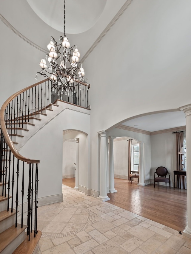 entrance foyer featuring an inviting chandelier, crown molding, ornate columns, a towering ceiling, and light hardwood / wood-style floors