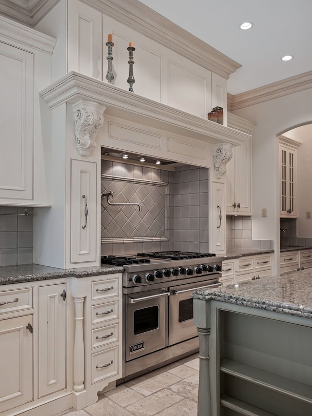 kitchen featuring backsplash, crown molding, dark stone counters, and double oven range