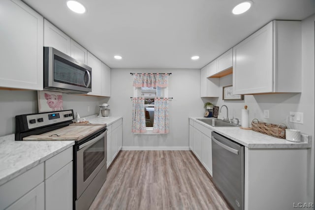 kitchen with white cabinets, light wood-type flooring, stainless steel appliances, and sink