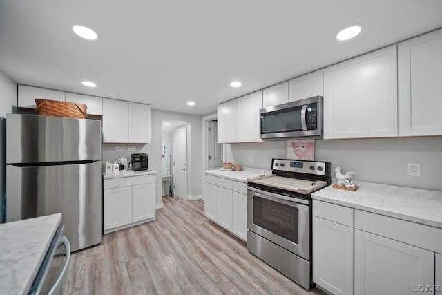 kitchen with white cabinets, appliances with stainless steel finishes, light wood-type flooring, and light stone countertops