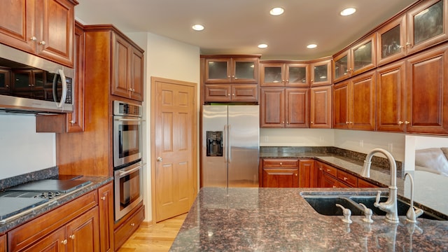 kitchen featuring dark stone countertops, light wood-type flooring, sink, and appliances with stainless steel finishes