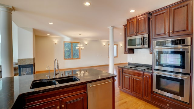 kitchen with light wood-type flooring, stainless steel appliances, sink, a notable chandelier, and dark stone countertops