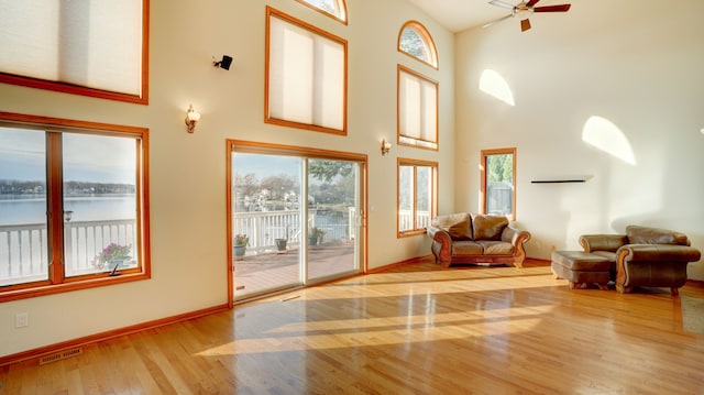 living room featuring a towering ceiling, a water view, ceiling fan, and light hardwood / wood-style floors