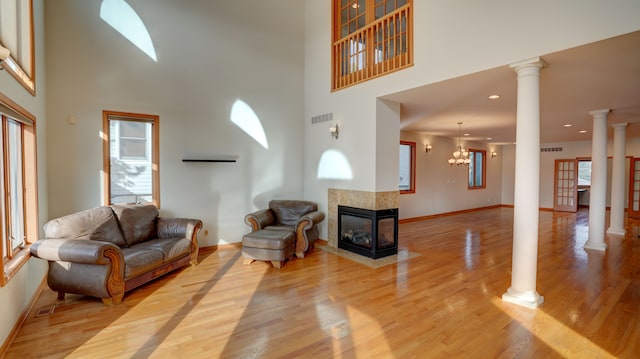 living room with decorative columns, light wood-type flooring, a towering ceiling, and a chandelier