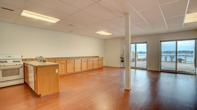 kitchen with a drop ceiling, kitchen peninsula, white appliances, a water view, and hardwood / wood-style flooring