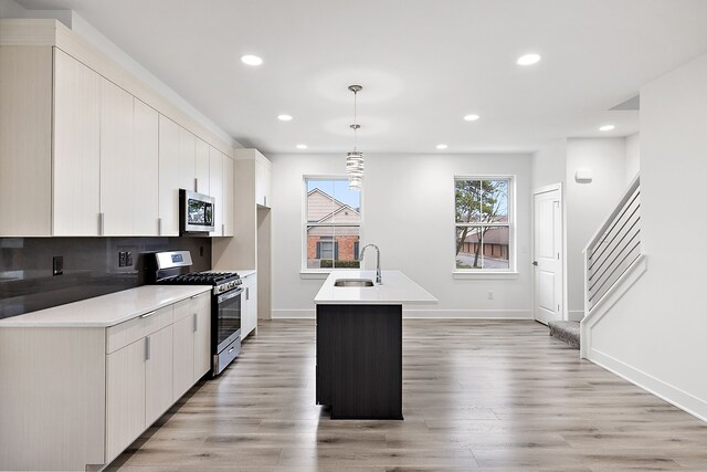 kitchen with pendant lighting, sink, light wood-type flooring, an island with sink, and appliances with stainless steel finishes