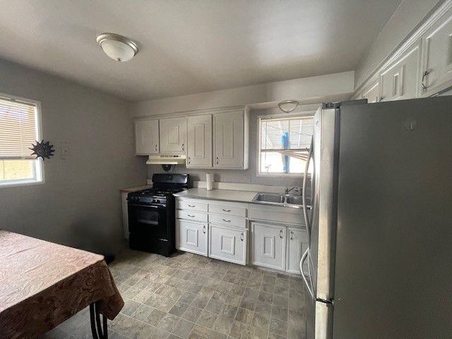 kitchen featuring black range, white cabinetry, sink, and stainless steel refrigerator