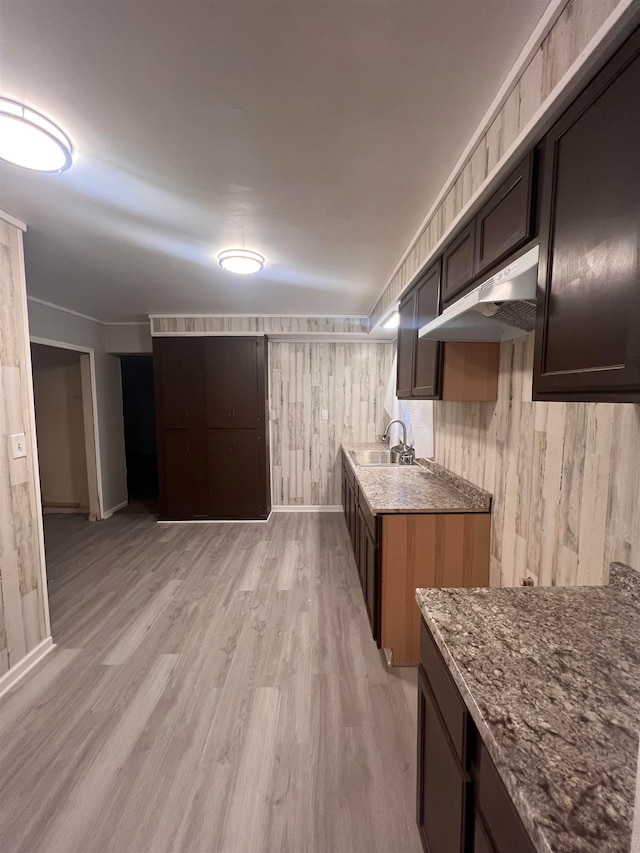 kitchen featuring dark brown cabinetry, wooden walls, light hardwood / wood-style flooring, and sink