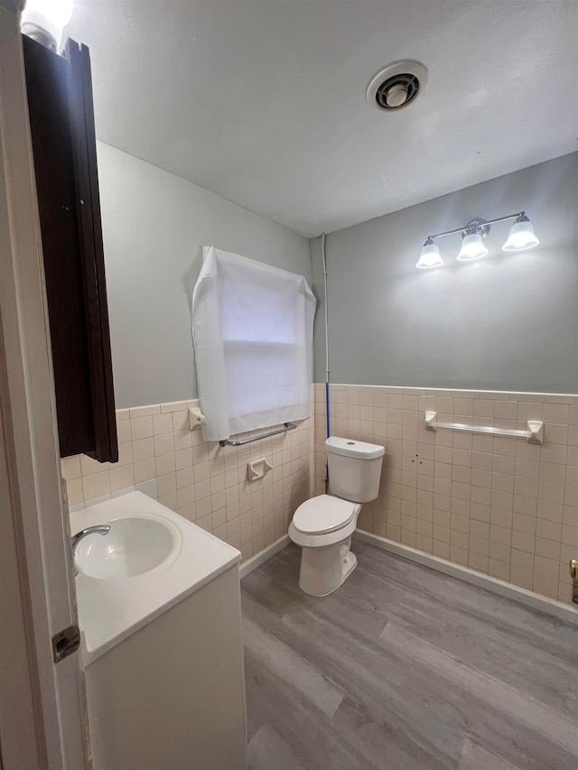 bathroom with hardwood / wood-style floors, vanity, toilet, and tile walls