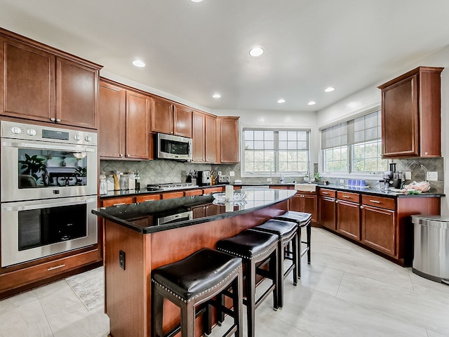 kitchen featuring light tile patterned flooring, decorative backsplash, appliances with stainless steel finishes, a kitchen island, and a breakfast bar area