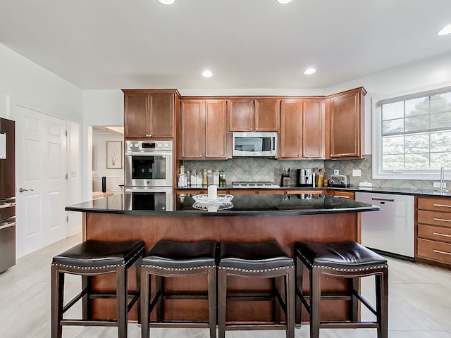 kitchen featuring light tile patterned flooring, backsplash, appliances with stainless steel finishes, a kitchen island, and a breakfast bar area