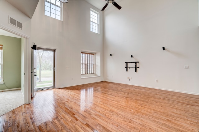 unfurnished living room featuring a towering ceiling, light hardwood / wood-style flooring, and ceiling fan