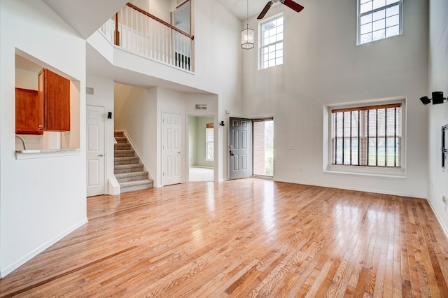 unfurnished living room with a wealth of natural light, ceiling fan, a high ceiling, and light hardwood / wood-style flooring