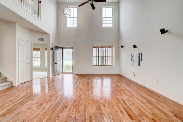 unfurnished living room with a high ceiling, light wood-type flooring, and ceiling fan