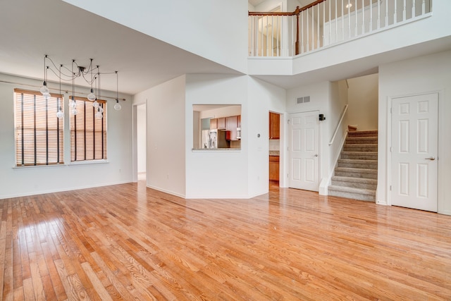 unfurnished living room featuring a towering ceiling and light wood-type flooring