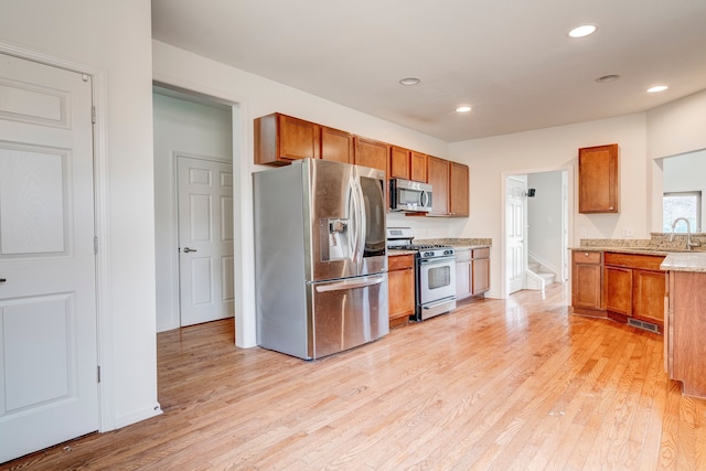 kitchen featuring light stone counters, light wood-type flooring, sink, and appliances with stainless steel finishes