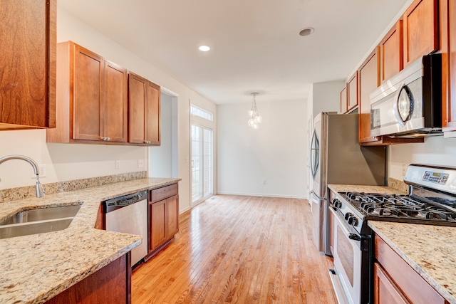 kitchen featuring light stone countertops, sink, decorative light fixtures, appliances with stainless steel finishes, and light wood-type flooring