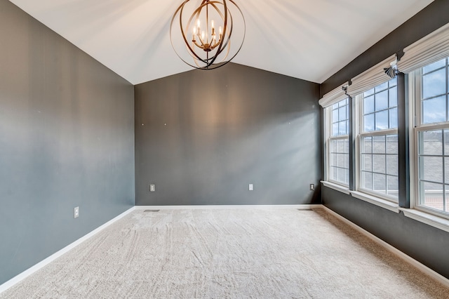 carpeted empty room featuring plenty of natural light, a chandelier, and vaulted ceiling