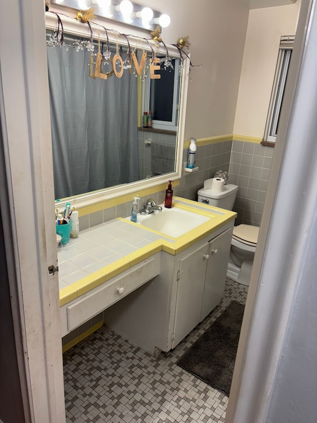 bathroom featuring tile patterned flooring, vanity, toilet, and tile walls