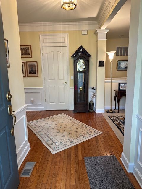 entryway featuring ornamental molding, ornate columns, and dark wood-type flooring