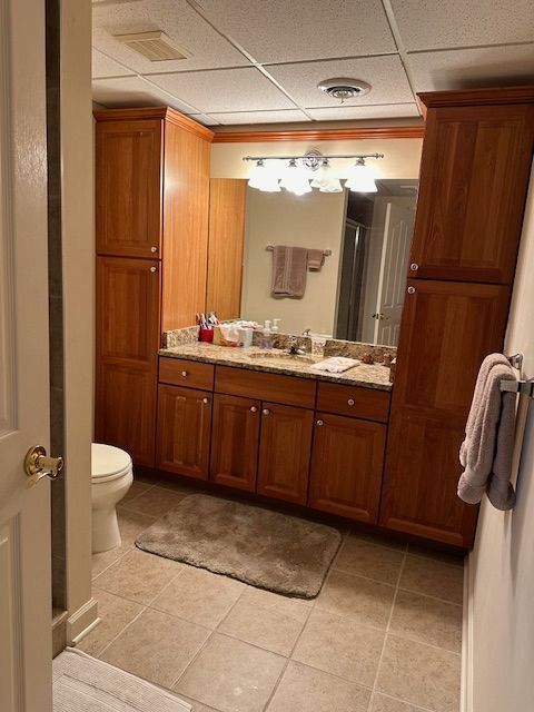 bathroom featuring a paneled ceiling, vanity, a shower, tile patterned flooring, and toilet