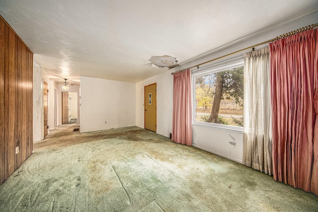 unfurnished room with ceiling fan, light carpet, and wooden walls