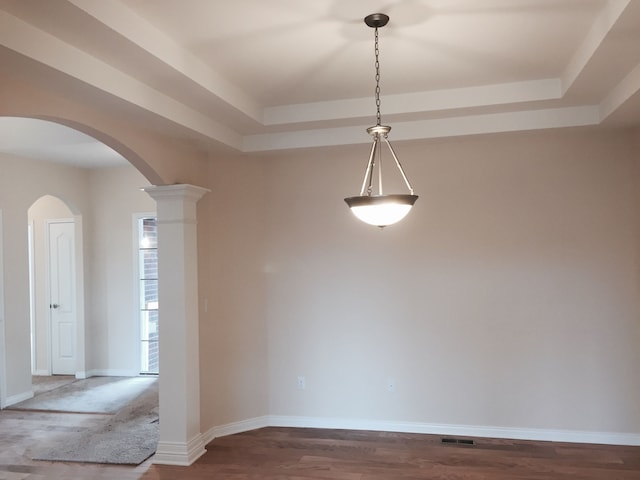 unfurnished dining area with a tray ceiling, decorative columns, and hardwood / wood-style floors