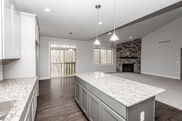 kitchen featuring decorative light fixtures, a kitchen island, light stone countertops, and a fireplace