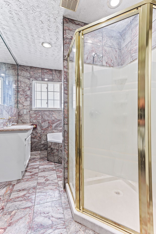 bathroom featuring shower with separate bathtub, vanity, a textured ceiling, and tile walls