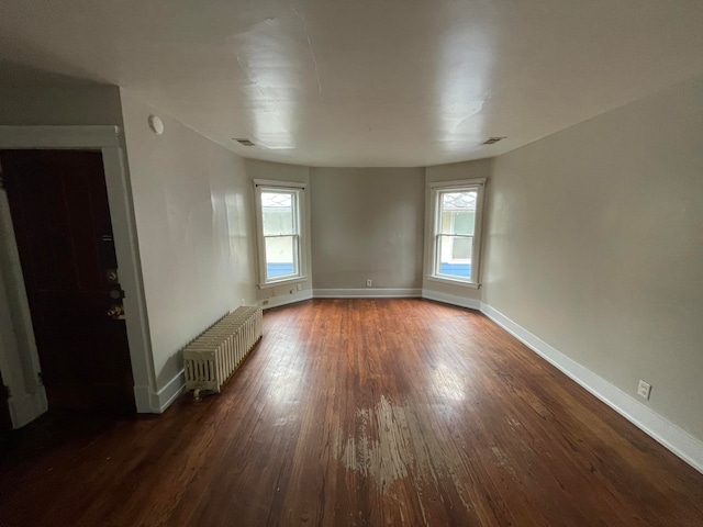 empty room with a wealth of natural light, dark hardwood / wood-style flooring, and radiator