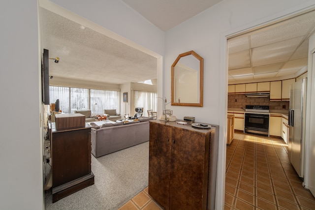 kitchen featuring a drop ceiling, white refrigerator with ice dispenser, electric stove, decorative backsplash, and dark tile patterned flooring