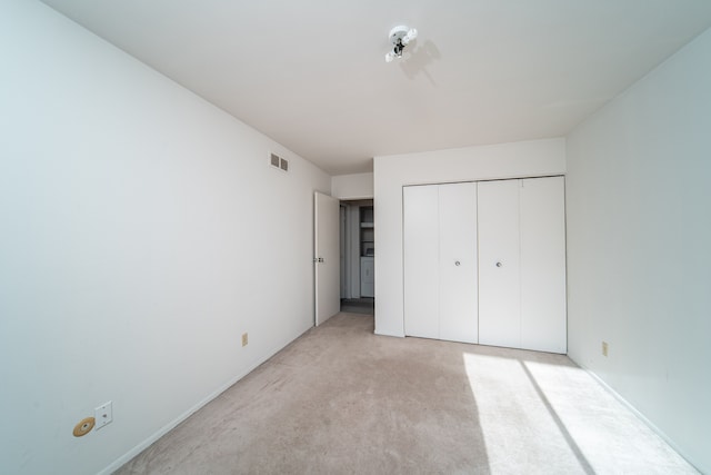 unfurnished bedroom featuring washer / dryer, light carpet, and a closet