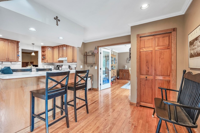 kitchen with a kitchen bar, kitchen peninsula, crown molding, pendant lighting, and light hardwood / wood-style flooring