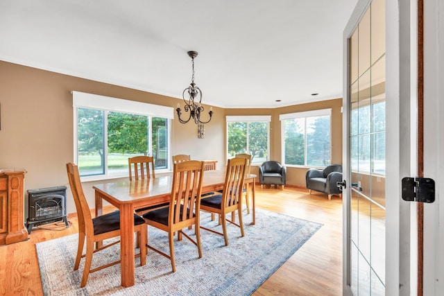 dining area with a notable chandelier, light wood-type flooring, crown molding, and a wood stove