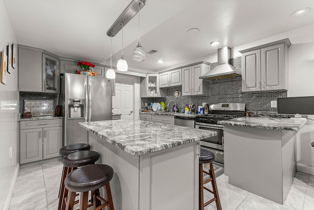 kitchen featuring wall chimney range hood, decorative backsplash, appliances with stainless steel finishes, a kitchen island, and a breakfast bar area