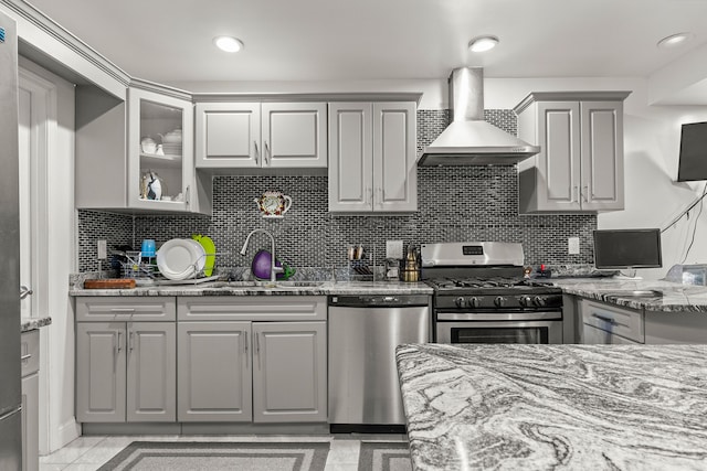 kitchen with light stone countertops, appliances with stainless steel finishes, sink, wall chimney range hood, and gray cabinets