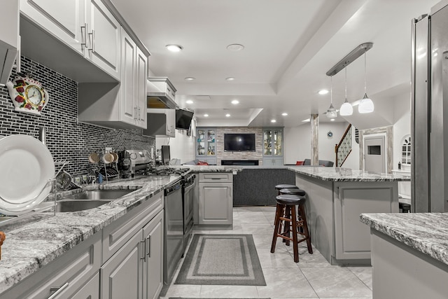 kitchen with light stone countertops, gray cabinets, a raised ceiling, and stainless steel gas range oven