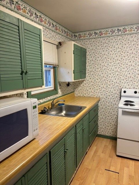 kitchen featuring light wood-style floors, a sink, white appliances, green cabinetry, and wallpapered walls