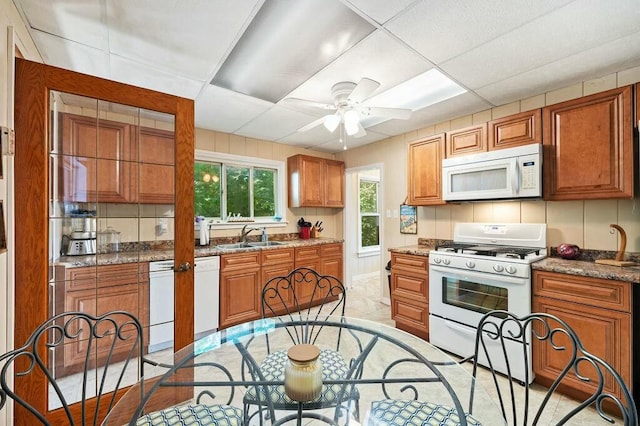 kitchen with backsplash, a paneled ceiling, white appliances, sink, and stone counters