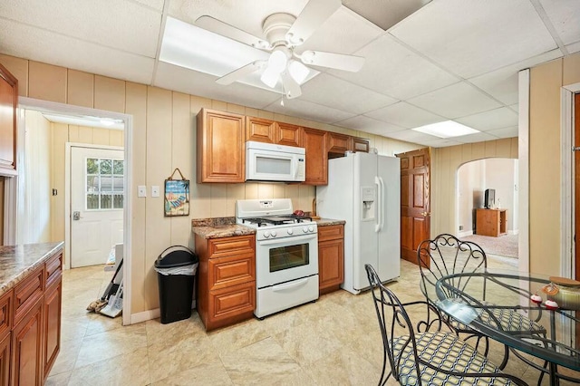 kitchen with light stone countertops, white appliances, a drop ceiling, and ceiling fan