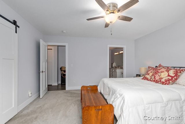 bedroom with a barn door, ceiling fan, ensuite bathroom, and light colored carpet