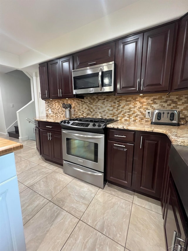 kitchen with tasteful backsplash, light stone countertops, dark brown cabinets, and appliances with stainless steel finishes