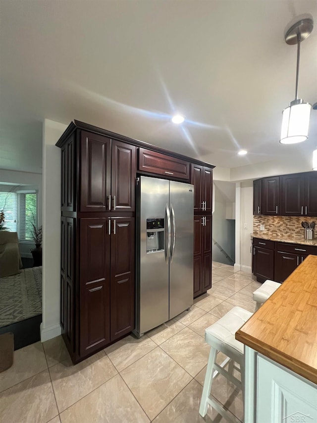 kitchen featuring stainless steel fridge with ice dispenser, decorative backsplash, dark brown cabinetry, decorative light fixtures, and butcher block counters