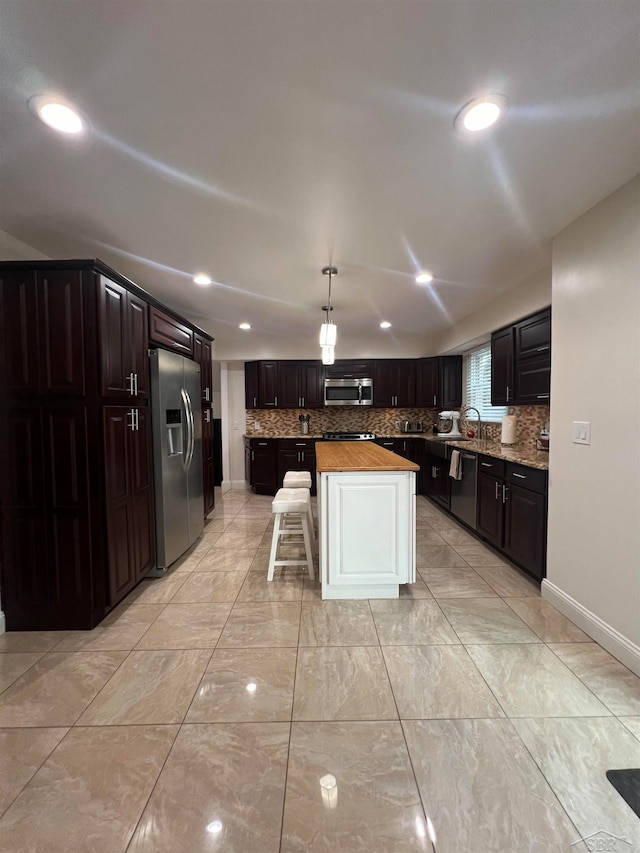 kitchen with wood counters, appliances with stainless steel finishes, tasteful backsplash, a center island, and hanging light fixtures