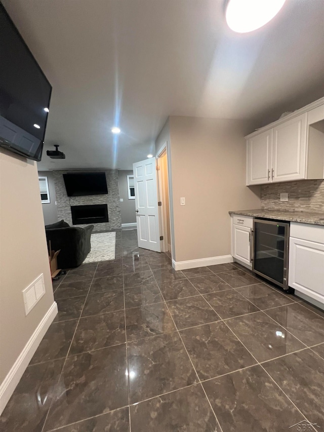 kitchen with light stone countertops, tasteful backsplash, a large fireplace, white cabinetry, and wine cooler